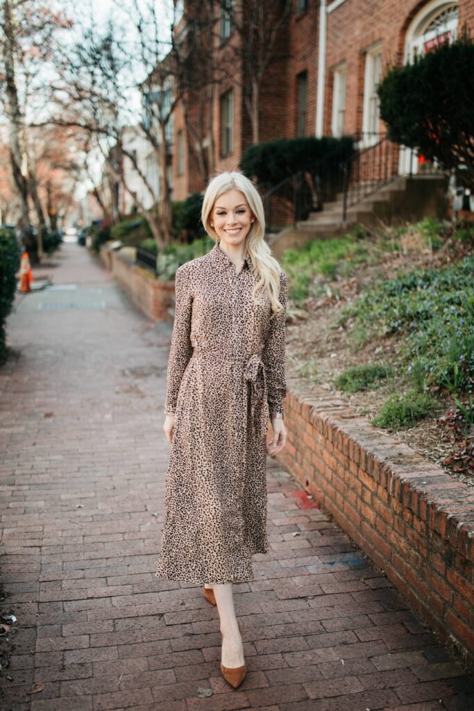Alison Cheperdak walking along a brick-lined city street in a neutral patterned dress and heels, embodying confidence and modern etiquette in everyday life.