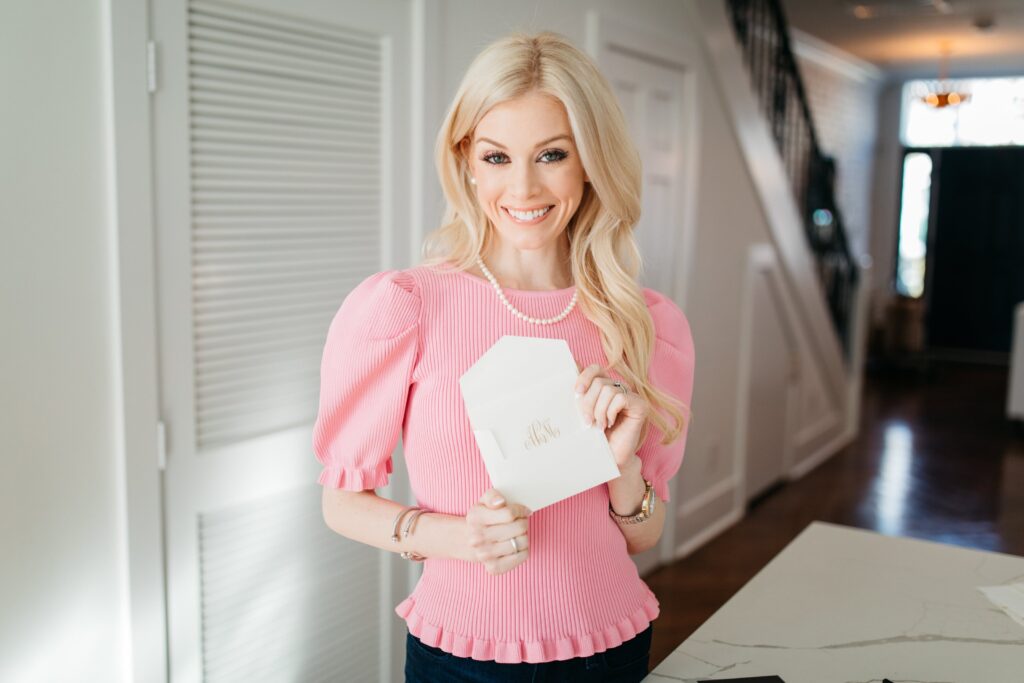 Alison Cheperdak smiling while holding an elegant envelope in a bright home setting, illustrating proper etiquette for written correspondence and thank-you notes.